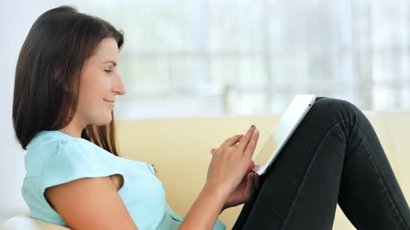 Young Woman is Relaxing on Comfortable Couch and Using Digital Tablet Indoors