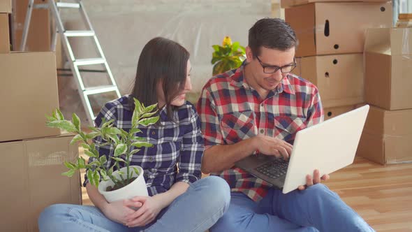 Couple with Laptop on the Background of Boxes for Moving New Home