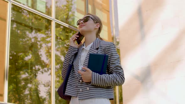 the Cheerful Student Walks By the University and Talks on the Phone