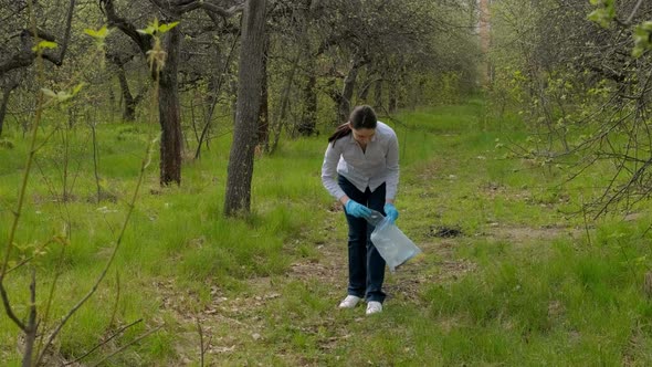 A Young Brunette Woman Collects Garbage in a Bag in the Park