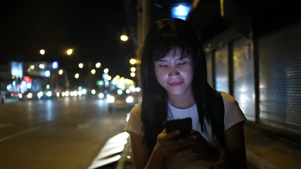 Asian woman smile and using a smartphone on a street in Downtown at night.