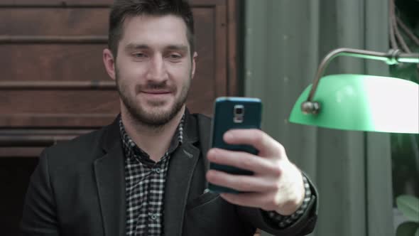 Young Man Sitting at the Desk and Taking Selfie on His Phone and Sending It