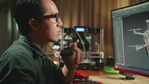 Asian Engineer Drinking Coffee While Work On Personal Computer And 3D Printer, Screen Shows 3D Drone
