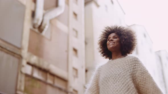 Smiling Young Woman With Windswept Afro Hair Walking Along Street
