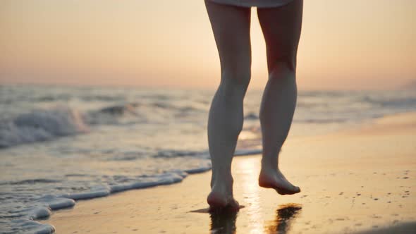 Happy barefoot woman running along the beach at sunset