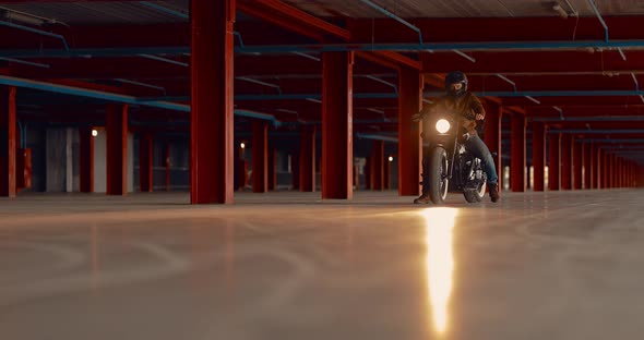 Tough Guy in a Helmet Starts to Ride a Motorcycle Through a Large Garage