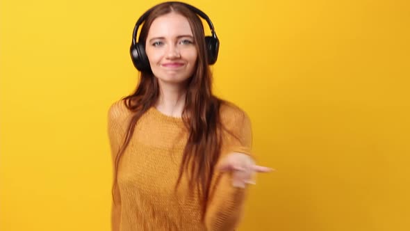 Woman Listening to Music in Black Headphones in the Studio on Pastel Yellow Background and Dancing