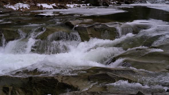 Rapid Flow of Water From a Mountain Creek and Stone Rapids with Snow in Winter. Waterfall. Slow