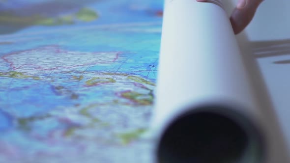 Man Unrolling World Map on Table, Tourist Planning Route for Vacation Abroad