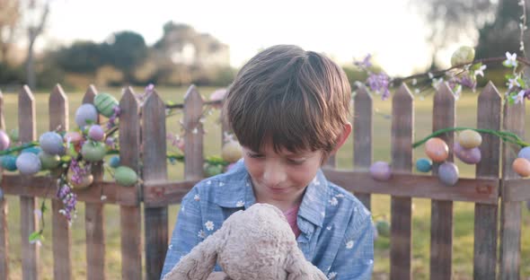 Close shot of a boy dressed in Easter attire playing with a stuffed Easter bunny.