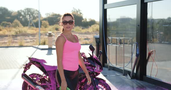 Female Biker in Glasses Dressed in Pink Top and Black Leather Trousers Poses on Camera