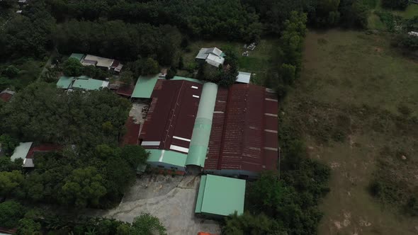 Aerial orbit shot of factory building in Cu Chi, Vietnam with farms, forests on sunny day with blue