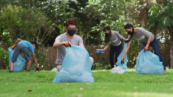 Asian parents, son and daughter wearing face masks holding refuse sacks collecting plastic waste