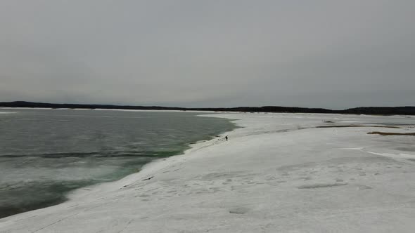 Aerial fly over edge of frozen lake with snow and ice