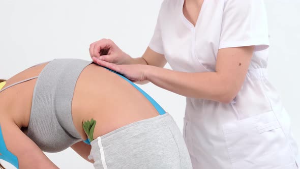 Physiotherapist sticks kinesio tapes to the small of the back of female patient, kinesiology taping