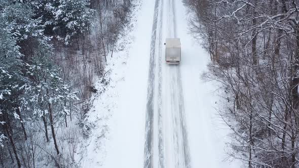 Aerial View of a Car Rides on a Road Surrounded By Winter Forest in Snowfall