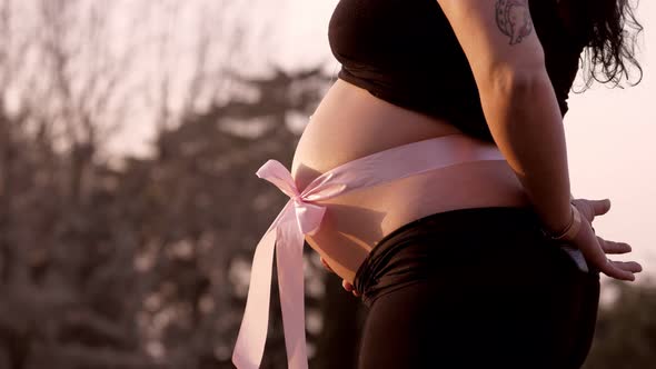 belly of a pregnant woman with a pink bow that heralds the birth of a baby girl