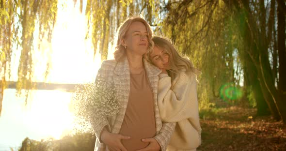 Pregnant Mother with Blonde Adult Daughter in Beige Clothes in Autumn Evening Park