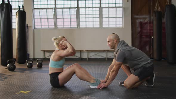 Fit caucasian woman performing crunches while male trainer holding her legs at the gym