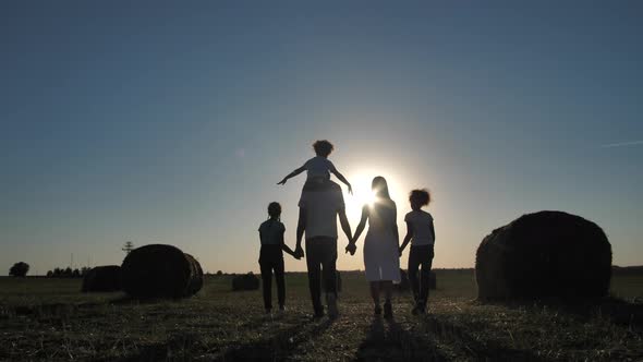 Multiethnic Family Walking Across Field at Sunset