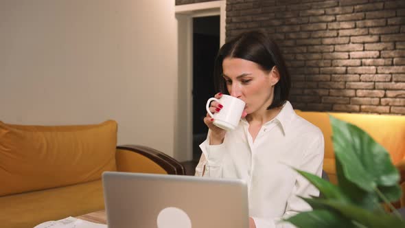 Pretty Caucasian Woman Drinking Coffee Using Laptop at Home Office