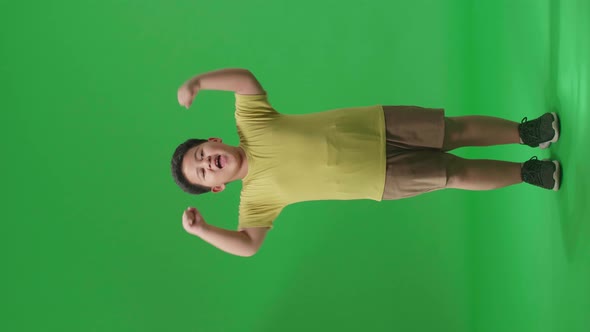 Full Body Of Cheerful Asian Little Boy Celebrating While Standing On Green Screen In The Studio