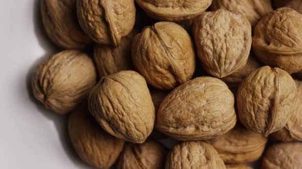 Cinematic, rotating shot of walnuts in their shells on a white surface - WALNUTS 