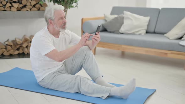 Old Man Using Smartphone on Yoga Mat at Home