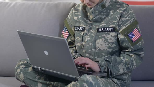Female American Soldier Browsing Internet Site by Laptop Sitting Sofa, Research