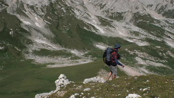 A man with a backpack on his back goes down a grassy mountain slope