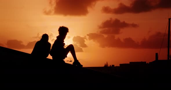 Silhouettes of a Couple Sitting on a Rooftop During Sunset