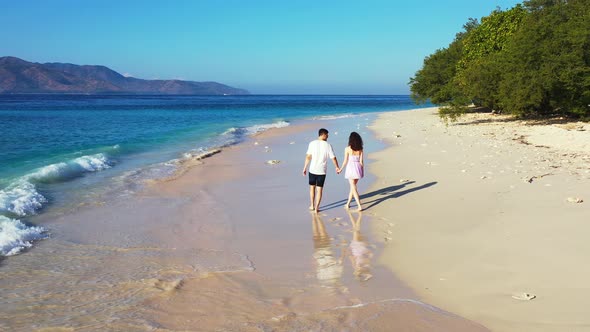 Couple holding hands, walking on beautiful exotic beach, rear wide view
