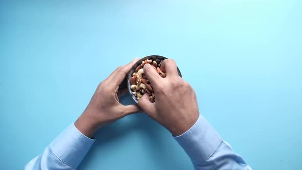 Top View of Hand Holding a Bowl of Mixed Nut on Blue Background