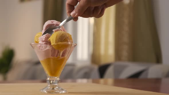 A man hand holding a spoon while eating delicious and tasty ice cream from a glass cup.
