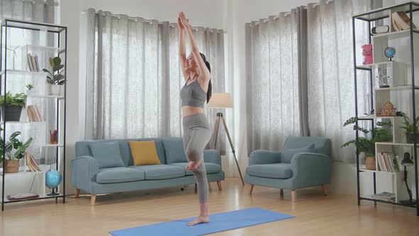 Young Asian Athletic Female In Sports Clothes Doing Yoga In Tree Pose On The Mat At Home