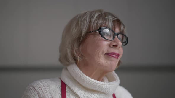 Headshot Portrait of Smiling Senior Woman in Eyeglasses Looking Out Window Indoors