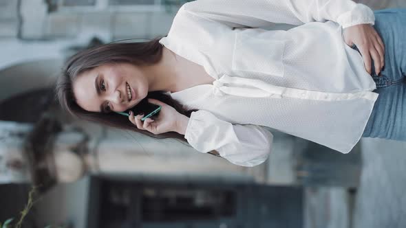 Beautiful Young Smiling Brunette Girl Talking on Her Smartphone, Standing Outdoors at Old