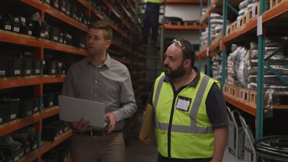 Two Caucasian male factory workers at a factory making hydraulic equipment in discussion