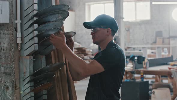 Man in a Carpentry Workshop Takes a Nozzle for Circular Saw From the Shelf