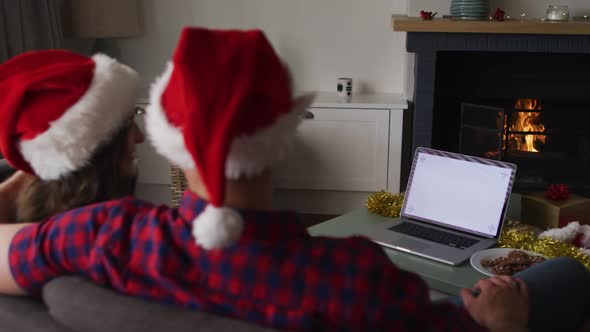 Back view of caucasian couple wearing santa hats using laptop with copy space on screen