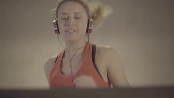 Close-up of Cheerful Sportswoman Jogging on Treadmill and Looking at Camera. Portrait of Young Blond