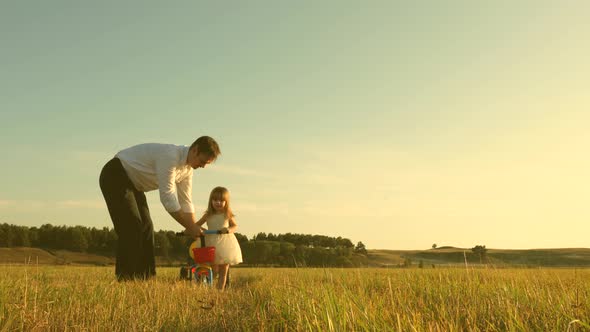 Happy Father Teaches Little Daughter To Ride a Bike. Dad Plays with Small Child on Lawn