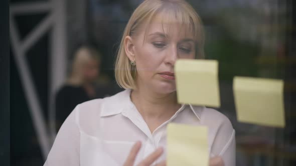 Concentrated Thoughtful Woman Writing with Pen on Adhesive Notes Planning Strategy Idea