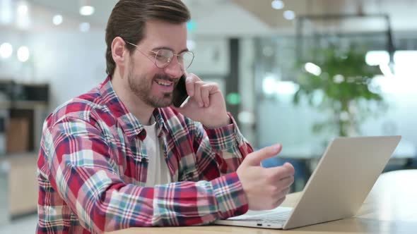 Hardworking Male Designer with Laptop Talking on Smartphone