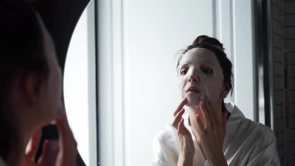 Woman in the Bathroom in Front of the Mirror Puts on a Rejuvenating Face Mask From Wrinkles