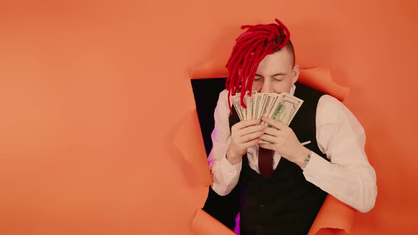 A Happy Young Man with Red Dreadlocks Sniffing Dollar Bills