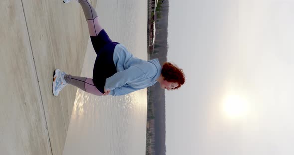 curly girl with red hair crouches on one leg and stretches her legs raising her hands up