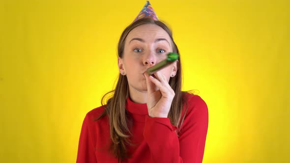 Young Woman in Birthday Hat That Is Blowing in Pipe Celebrating Over Yellow Background