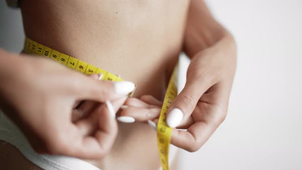 A Girl is Measuring Her Waist with a Centimeter Tape