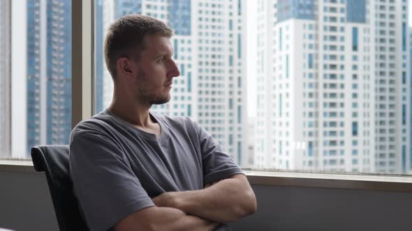 A Pensive Young in an Office Looking to the Window at the Office Buildings in Downtown